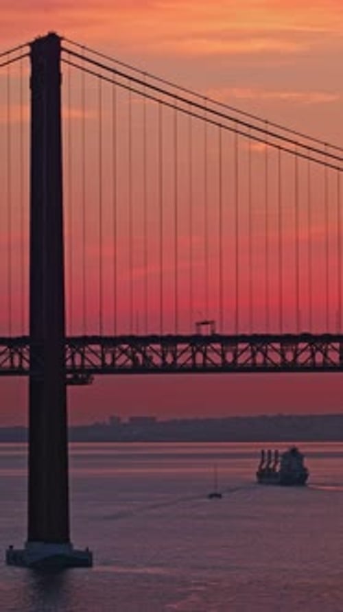 Cargo Ship Passing Under 25 De Abril Bridge at Sunset Lisbon Portugal