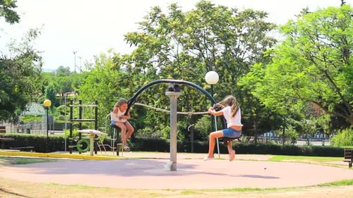 Two little girls in the park, spinning on a round seesaw, having fun
