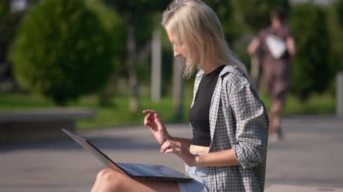 Beautiful young freelance woman with laptop lying sitting on bench in park.
