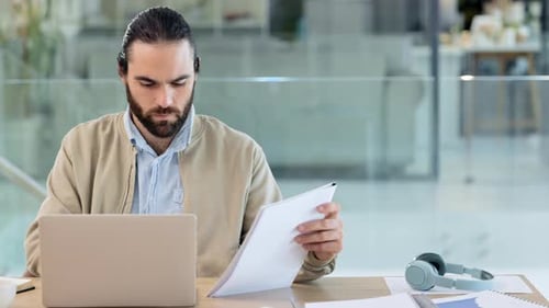 Trendy business man reading reports, typing notes on a laptop in an office
