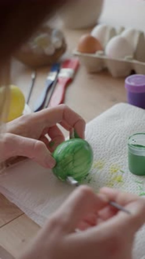 Woman painting Easter egg at home with pastel paints