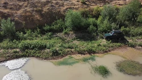 Vue aérienne d'un véhicule tout-terrain circulant dans une zone verte près d'un ruisseau