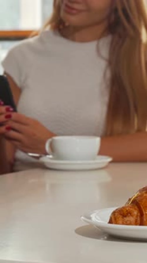 Woman Uses Phone at Restaurant with Coffee and Pastries