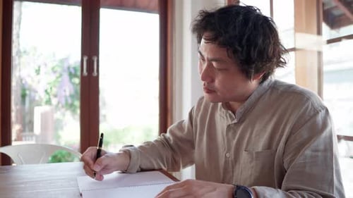 Asian man writing idea plan on a notebook in a cafe