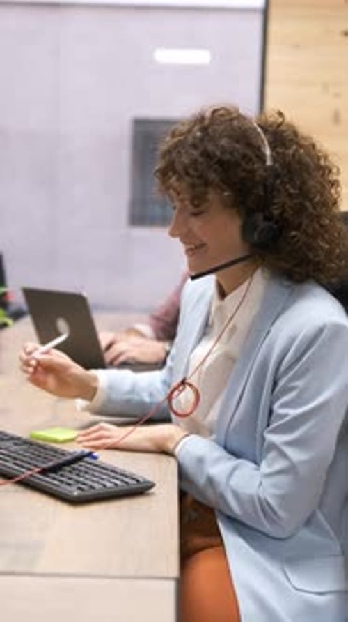 Woman Wearing Headset Writing at Computer in Office