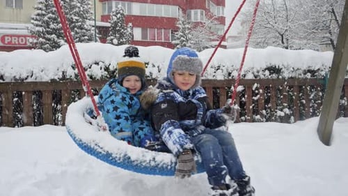 Two brothers happily playing on a snowy swing set at the public playground