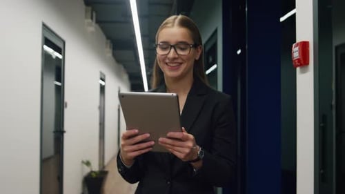 Smiling businesswoman touching tablet walking office hallway confident in her work