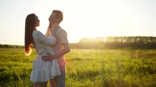 Happy Young Couple in Love Hugging Kissing and Holding Hands on Background of Sunset in Summer Field