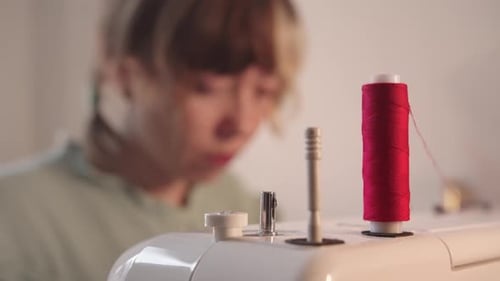 Woman Sewing with Red Thread on Sewing Machine