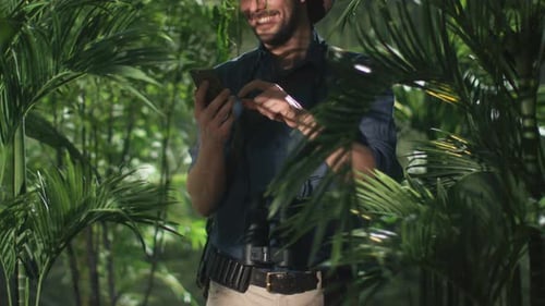 Adventurer in Hat using Mobile Phone in Jungle Forest.