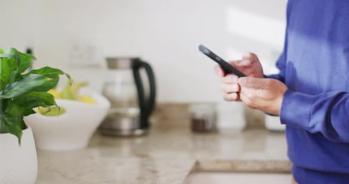 Video of midsection of senior biracial man using smartphone in kitchen