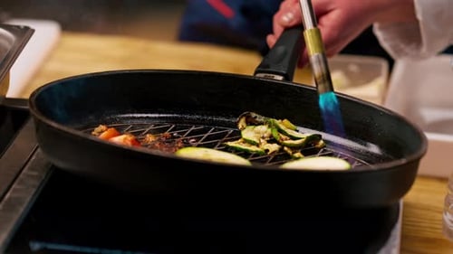 Close Up Chef Frying Different Vegetables on a Hot Frying Pan with Torch on the Stove