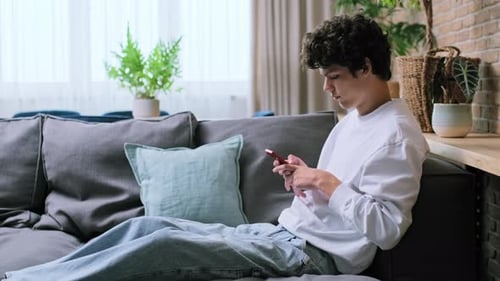 Young Man Using Phone Relaxing on Couch at Home