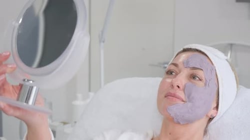 Woman with Lavender Facial Mask Looks in Mirror