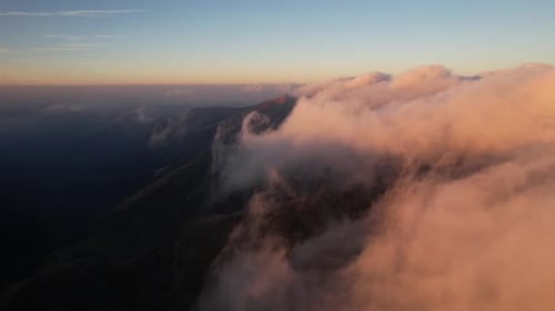 Aerial view of clouds embracing mountain peaks during a stunning golden hour sunrise