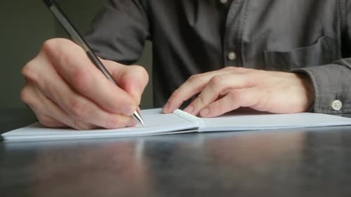 Close-up of Man Writing in Notebook on Desk