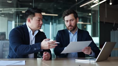 Coworkers in Formal Clothes Sitting By Desk with Laptop and Analyzing Document
