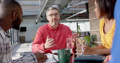 Team of diverse colleagues discussing while sitting on a table together at office
