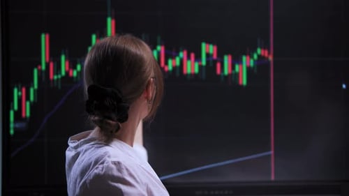 Young Woman Wearing Glasses Studying Financial Data on Interactive Screen