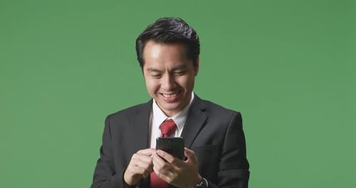 An Asian Business Man Enjoy Using Mobile Phone While Standing On Green Screen In The Studio