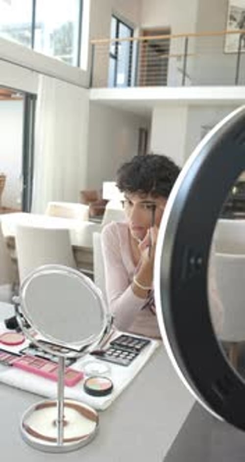 Vertical video: Applying makeup at home, person using brush with ring light and mirror