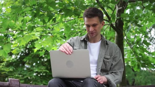 a young male freelancer works at his laptop in the park.
