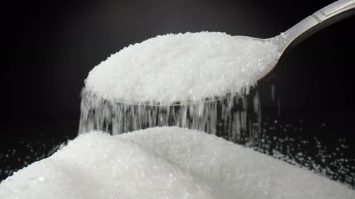 White sugar delicately tumbles off a spoon