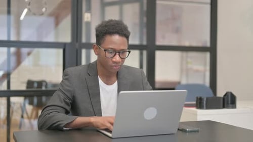 African American Man Looking at Camera while Working on Laptop in Office