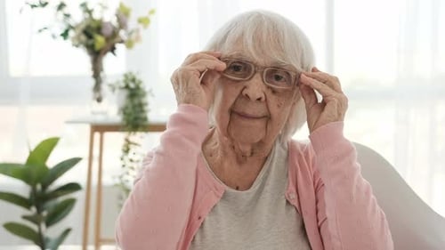 Senior Woman Puts on Her Eyeglasses Indoors