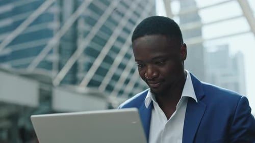 Portrait of African American Man Manager Works on Laptop Against Skyscraper