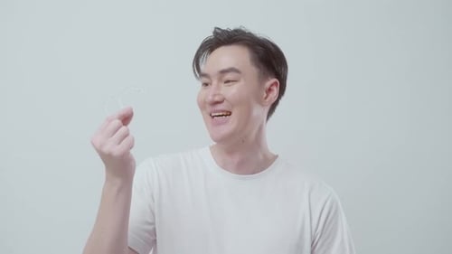 Young smiling man holding Invisalign braces over white background studio