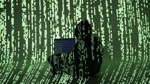 Hacker silhouetté en sweat à capuche travaillant sur un ordinateur portable entouré d'un code vert en chute projetée