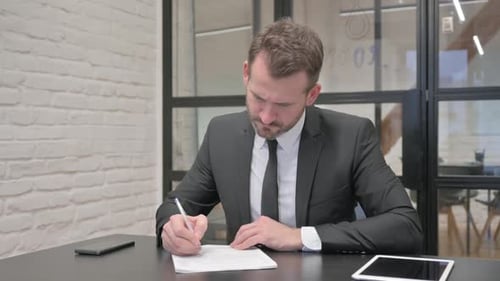 Man Writing on Paper at Business Office Desk