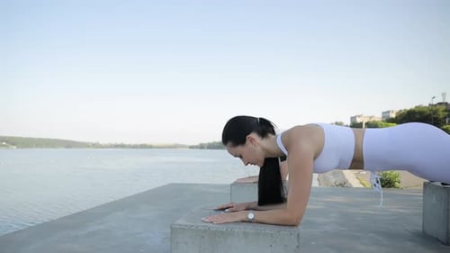 Two Women Do the Plank Exercise on Large Stones on the Embankment of a Pond a Lake