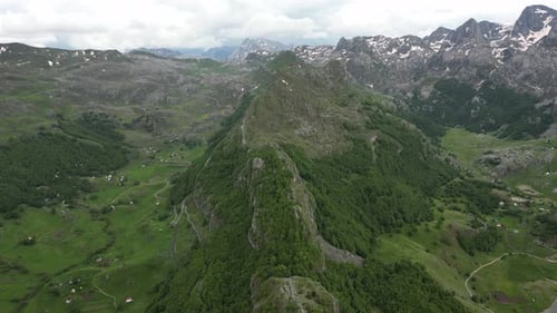 Flying over beautiful green mountains. In the background, stone cliffs with snow are visible.