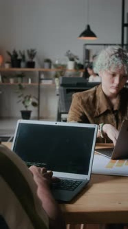 Male Programmer Coding on Laptop at Shared Desk in Office