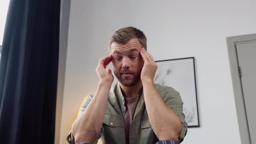 Man Massaging Temples Experiencing a Headache Indoors