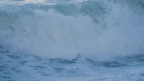Close Up of Sea Waves Breaking onto Beach in Slow Motion with Sun Reflection on Water