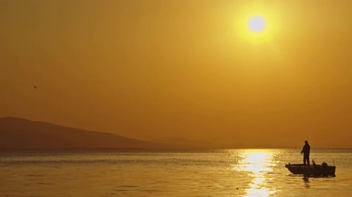 Fischer, der mit einer Angelrute in einem Boot im Meer bei gelbem Sonnenuntergang fischt