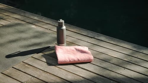 Yoga mat, water bottle, and towel on wooden deck by pool, copy space