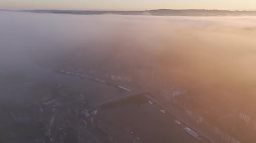 Aerial view of foggy river city with bridge and boats, Dinant, Belgium.