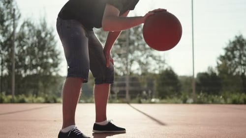 Man Dunks Ball with Hand on Outdoor Basketball Court on Sunny Picturesque Day