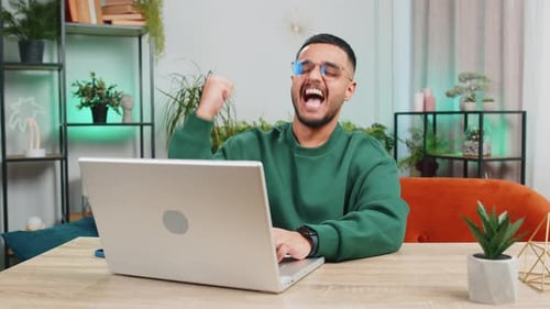Man Celebrates Success on Laptop at Home