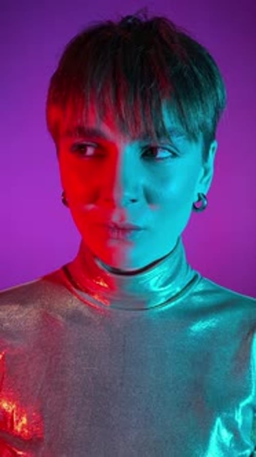 Vertical portrait young woman blinks, glances in neon light indoors