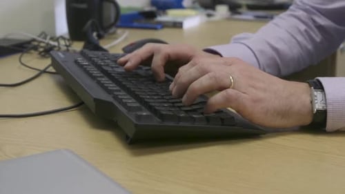 Male office worker hands typing on computer keyboard close up dolly right across desk.