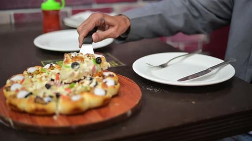 Young man is bringing piece of pizza from plate to face. He is resting in a pizzeria .
