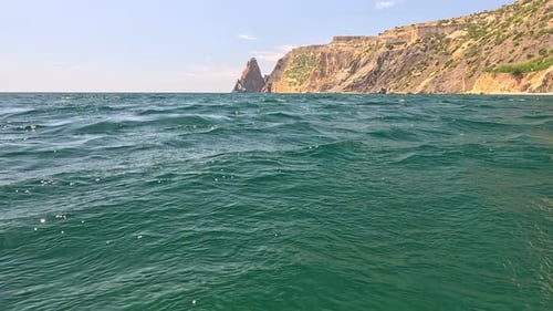 Sea Water Surface Camera Flies Over the Calm Azure Sea with Volcanic Rocky Shores on Background