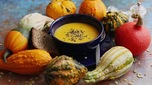 Vegetarian Autumn Pumpkin Cream Soup with Seeds and Colorful Various Mini Pumpkins Around