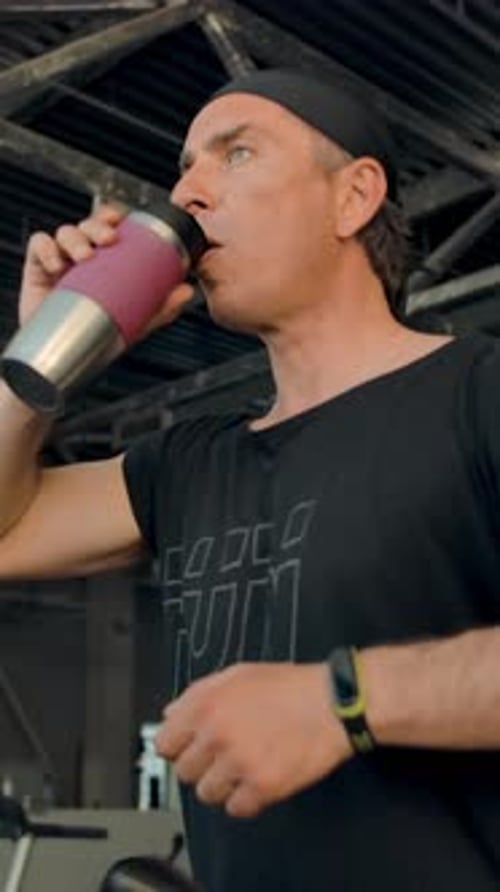 Vertical of Portrait of an Aged Man Running on a Treadmill He Pulls Out a Glass of Water