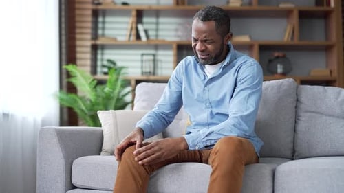 Man Holding Knee in Pain While Sitting on Couch